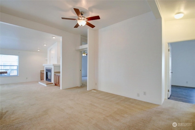 unfurnished living room featuring light colored carpet, a fireplace with raised hearth, and ceiling fan