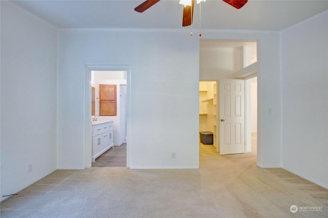 unfurnished bedroom with light carpet, connected bathroom, ceiling fan, a walk in closet, and a sink