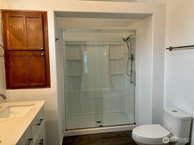 bathroom with wood finished floors, a shower stall, toilet, and vanity