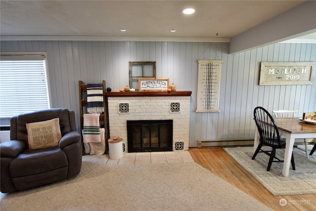 living room featuring baseboard heating, wood-type flooring, and a brick fireplace