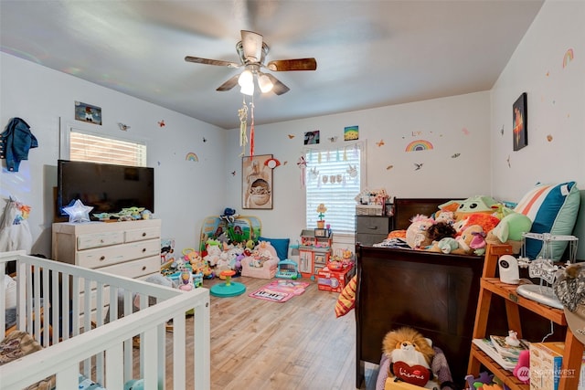 bedroom with a nursery area, ceiling fan, and wood-type flooring