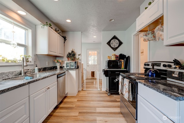 kitchen featuring appliances with stainless steel finishes, white cabinetry, sink, light hardwood / wood-style floors, and a textured ceiling