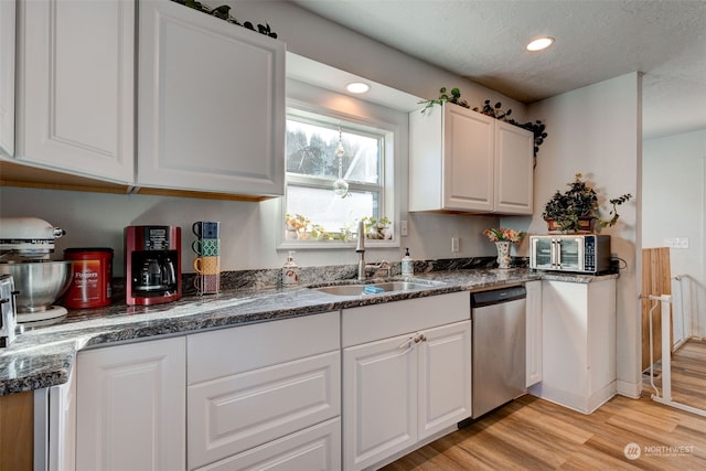 kitchen featuring sink, dark stone countertops, light hardwood / wood-style floors, white cabinets, and stainless steel dishwasher