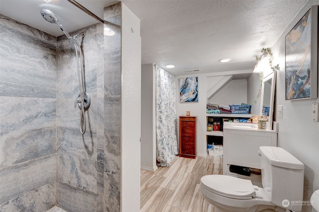 bathroom featuring vanity, tiled shower, a textured ceiling, and toilet