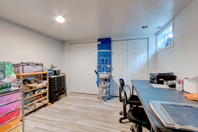 home office with light hardwood / wood-style floors and a textured ceiling