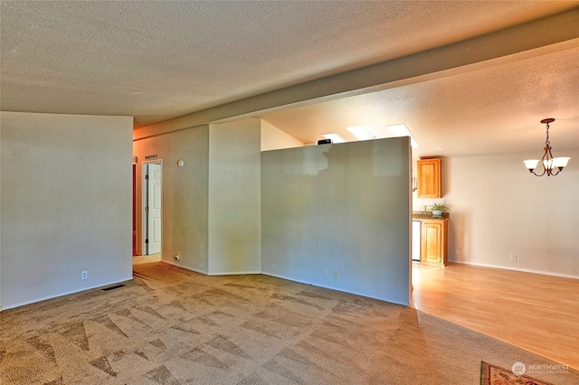 empty room with lofted ceiling, a notable chandelier, a textured ceiling, and carpet flooring