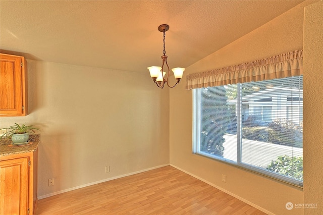 unfurnished dining area with vaulted ceiling, a textured ceiling, a notable chandelier, and light hardwood / wood-style floors