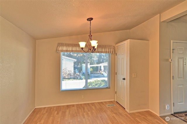 unfurnished dining area featuring hardwood / wood-style flooring, an inviting chandelier, vaulted ceiling, and a textured ceiling