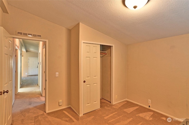 unfurnished bedroom featuring vaulted ceiling, carpet flooring, a textured ceiling, and a closet