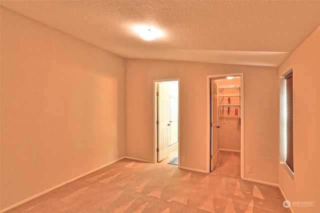 unfurnished bedroom featuring vaulted ceiling, carpet, a spacious closet, ensuite bath, and a closet