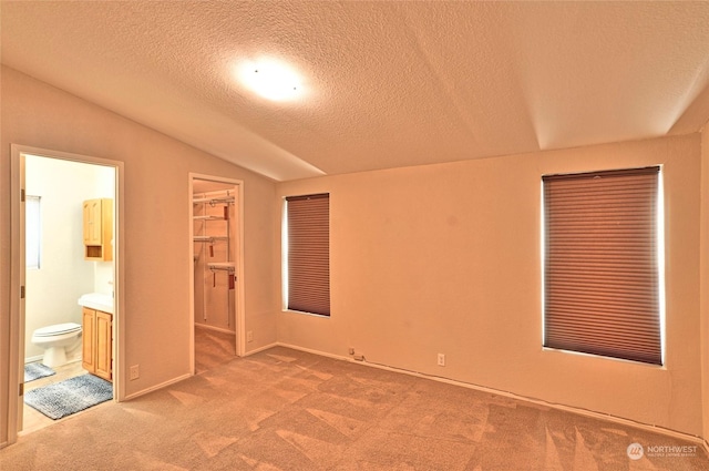 unfurnished bedroom with lofted ceiling, carpet, connected bathroom, a textured ceiling, and a walk in closet