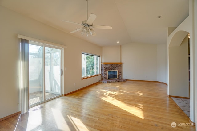 unfurnished living room featuring lofted ceiling, a brick fireplace, and light wood-type flooring