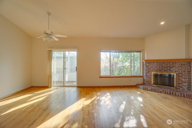 unfurnished living room featuring plenty of natural light, lofted ceiling, light wood-type flooring, and a brick fireplace