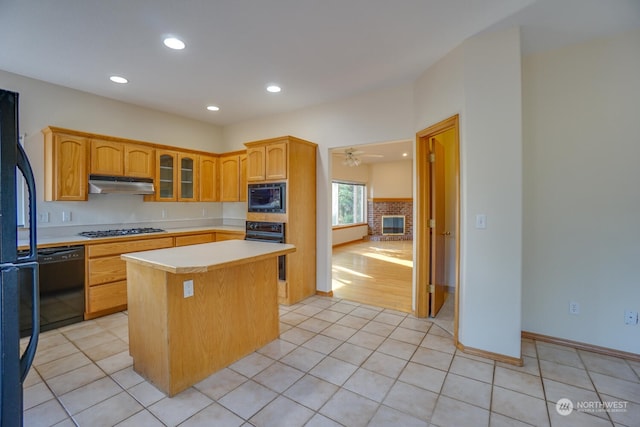 kitchen with a brick fireplace, light tile patterned flooring, a kitchen island, and black appliances