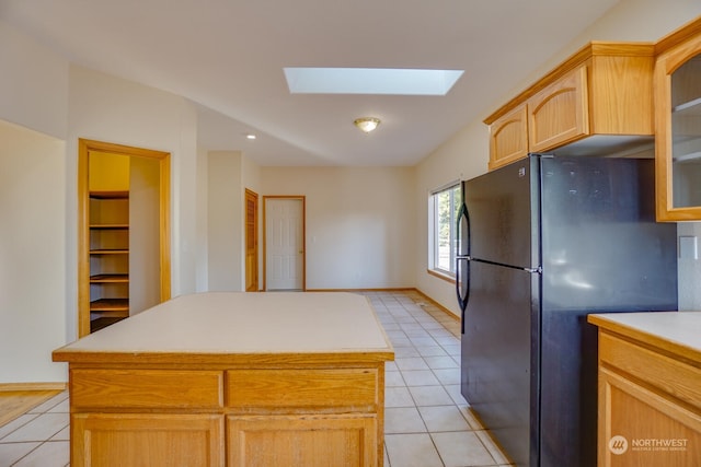 kitchen featuring black refrigerator, a skylight, a center island, and light brown cabinets