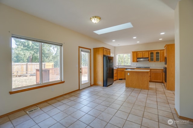 kitchen with sink, a skylight, light tile patterned floors, a kitchen island, and black appliances