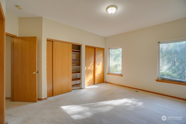 unfurnished bedroom with multiple closets and light carpet