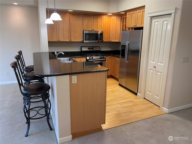 kitchen with a kitchen bar, sink, decorative light fixtures, appliances with stainless steel finishes, and kitchen peninsula