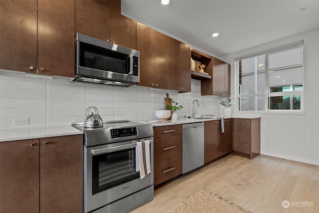 kitchen featuring tasteful backsplash, stainless steel appliances, sink, and light wood-type flooring