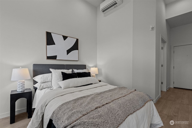 bedroom with a wall mounted air conditioner, a high ceiling, and light wood-type flooring