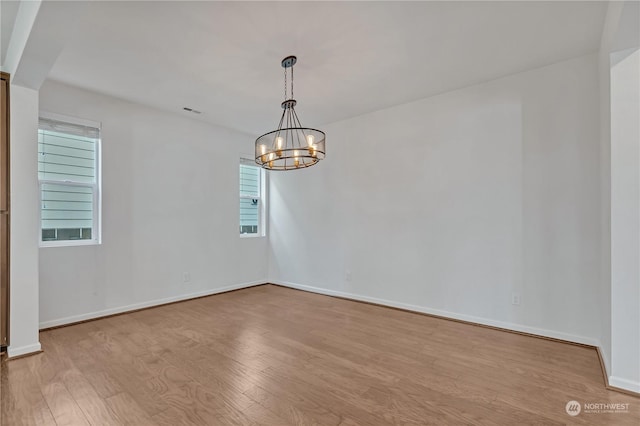 empty room featuring an inviting chandelier and light hardwood / wood-style floors