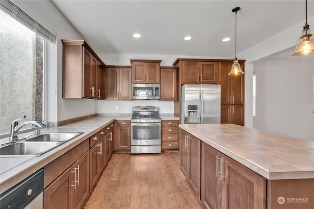 kitchen featuring sink, decorative light fixtures, tile counters, stainless steel appliances, and light hardwood / wood-style floors