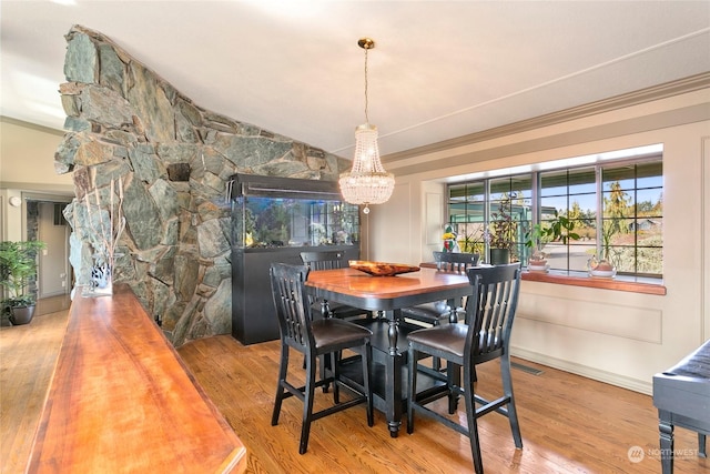 dining room featuring an inviting chandelier, ornamental molding, wood-type flooring, and vaulted ceiling