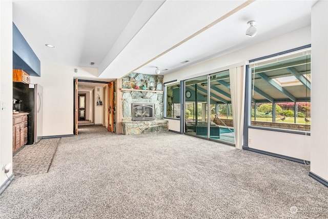 unfurnished living room featuring a stone fireplace and carpet floors