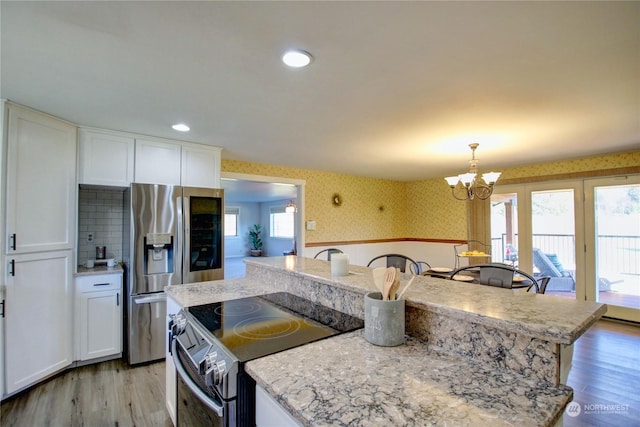 kitchen featuring white cabinetry, hanging light fixtures, appliances with stainless steel finishes, a kitchen island, and light stone countertops