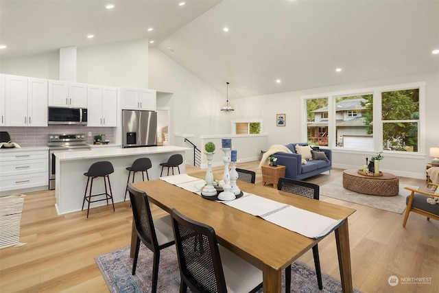 dining area featuring high vaulted ceiling, recessed lighting, light wood-style flooring, and an inviting chandelier