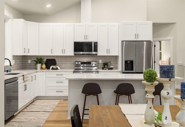 kitchen with sink, white cabinetry, appliances with stainless steel finishes, light hardwood / wood-style floors, and decorative backsplash