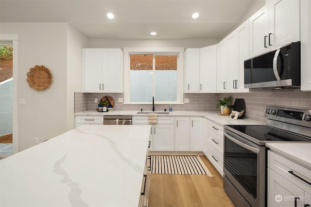 kitchen featuring sink, light hardwood / wood-style flooring, appliances with stainless steel finishes, white cabinetry, and backsplash