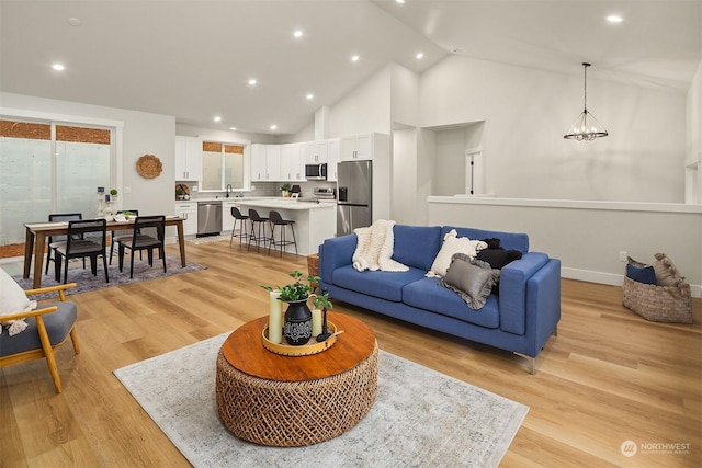 living room with high vaulted ceiling, sink, and light wood-type flooring