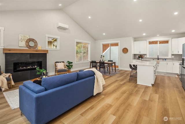 living room with high vaulted ceiling, light hardwood / wood-style floors, sink, and an AC wall unit