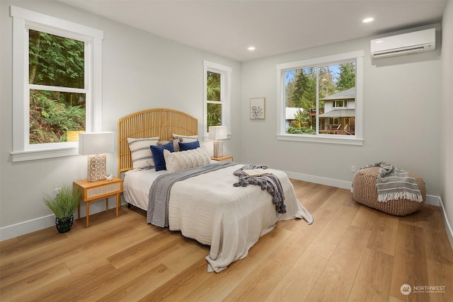 bedroom featuring multiple windows, a wall unit AC, and light hardwood / wood-style floors