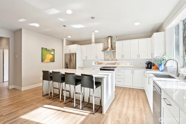 kitchen with stainless steel appliances, a sink, light countertops, wall chimney range hood, and a center island