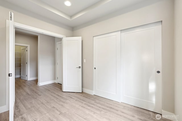 unfurnished bedroom with light wood-type flooring, a closet, and baseboards