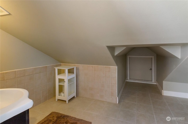 bathroom with vaulted ceiling, tile patterned flooring, and tile walls