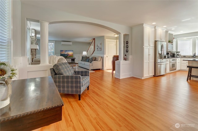 living room featuring light hardwood / wood-style floors, decorative columns, and an AC wall unit