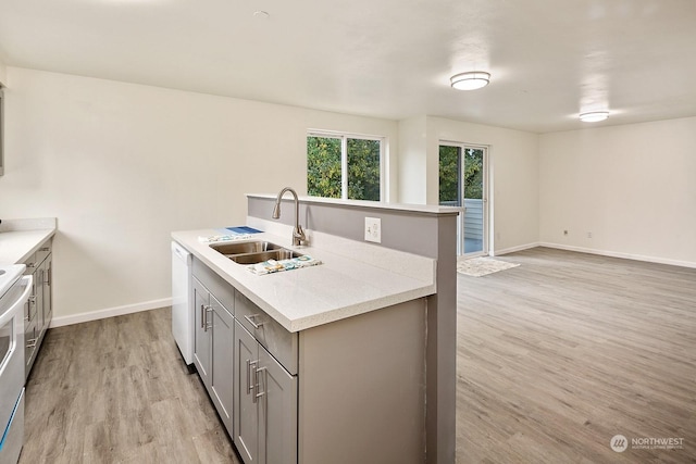 kitchen with gray cabinets, sink, a kitchen island with sink, white dishwasher, and light wood-type flooring