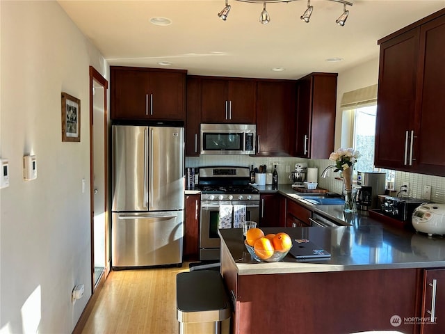 kitchen with sink, decorative backsplash, kitchen peninsula, stainless steel appliances, and light wood-type flooring