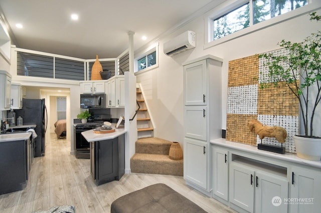 kitchen featuring gas range, a wall mounted air conditioner, light wood-type flooring, decorative backsplash, and white cabinets