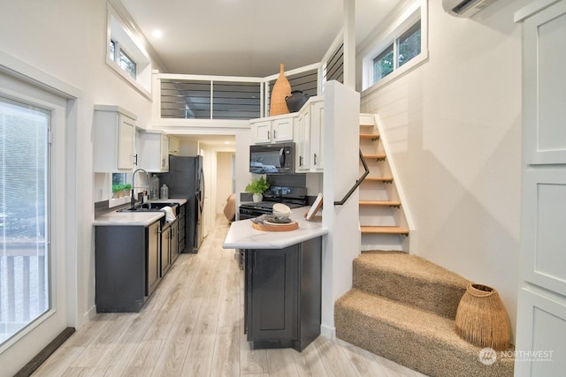 kitchen with white cabinetry, a healthy amount of sunlight, light wood-type flooring, and black appliances