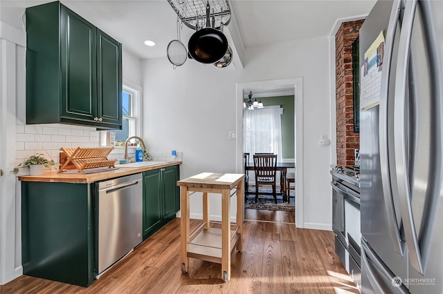 kitchen featuring tasteful backsplash, sink, green cabinets, stainless steel appliances, and light hardwood / wood-style flooring