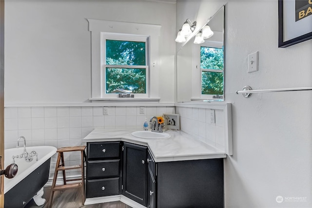 bathroom with a healthy amount of sunlight, a tub to relax in, vanity, and tile walls