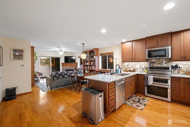 kitchen with sink, appliances with stainless steel finishes, hanging light fixtures, kitchen peninsula, and light wood-type flooring