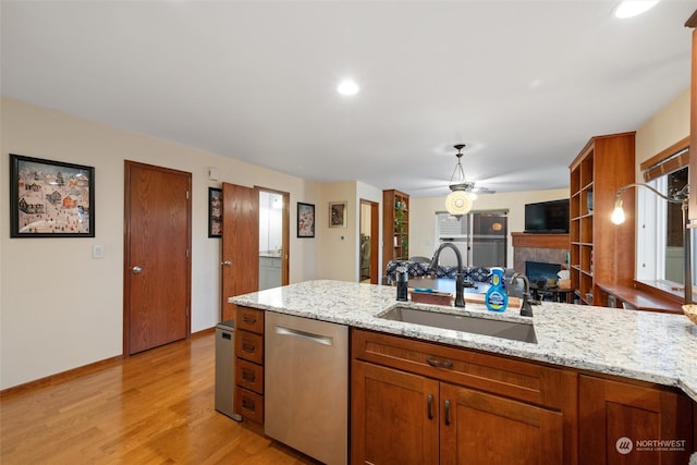 kitchen with stainless steel dishwasher, light stone countertops, sink, and a tile fireplace