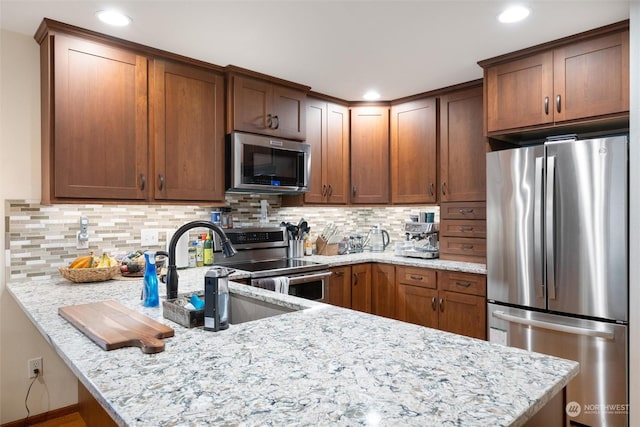 kitchen featuring light stone counters, stainless steel appliances, kitchen peninsula, and backsplash