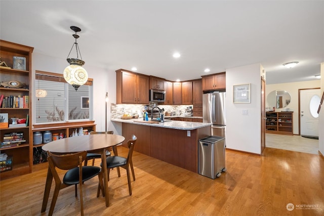 kitchen with light hardwood / wood-style flooring, appliances with stainless steel finishes, hanging light fixtures, tasteful backsplash, and kitchen peninsula