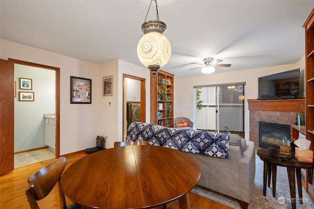 dining room featuring washer / clothes dryer, a tile fireplace, ceiling fan, and light wood-type flooring